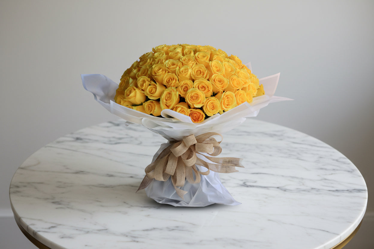 Bouquet of yellow roses wrapped in white paper with a beige ribbon on a white background