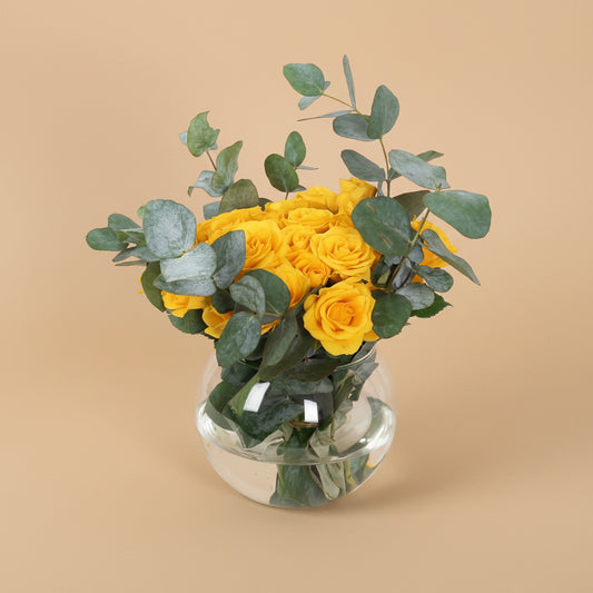 Bouquet of yellow roses with greenery in a clear glass vase on a white background