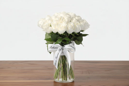 Bouquet of white roses in a clear vase with a white ribbon on a light gray background