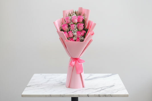 Bouquet of pink roses wrapped in pink paper held by a person.