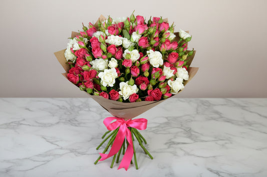 Bouquet of pink and white flowers with a pink ribbon on a wooden surface.