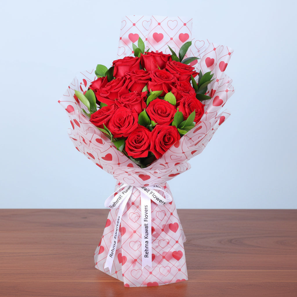 Bouquet of red roses wrapped in tissue paper with heart patterns on a light blue background.