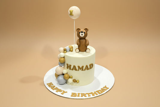 Birthday cake with teddy bear decoration and 'Happy Birthday' text on a white background.